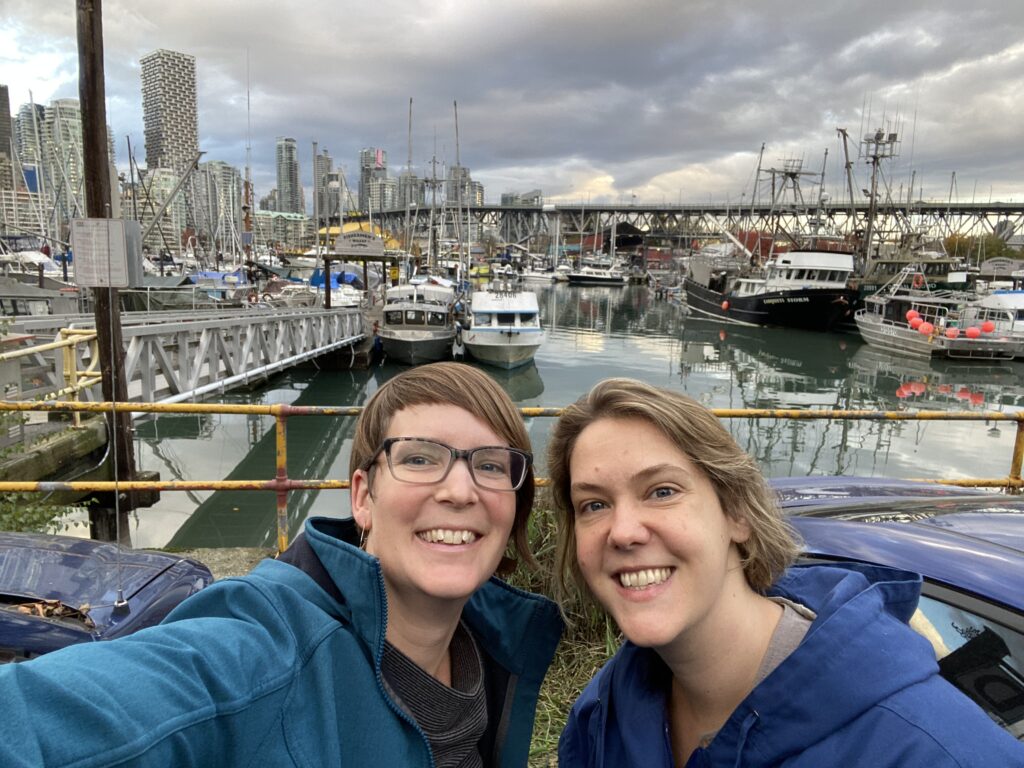 Two women standing outdoors taking a selfie in front of a harbour