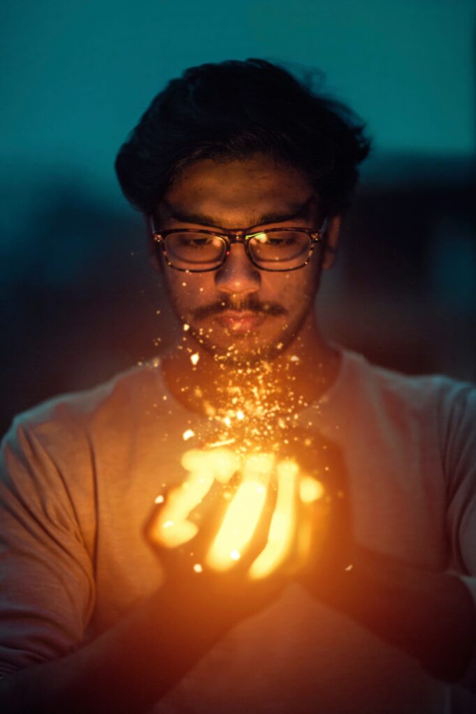 Masculine person with glasses holding sparkling embers that look magical