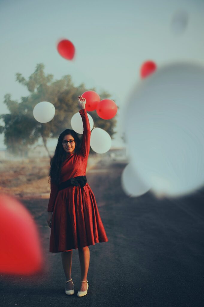 A woman in a red dress surrounded by red and white balloons floating away