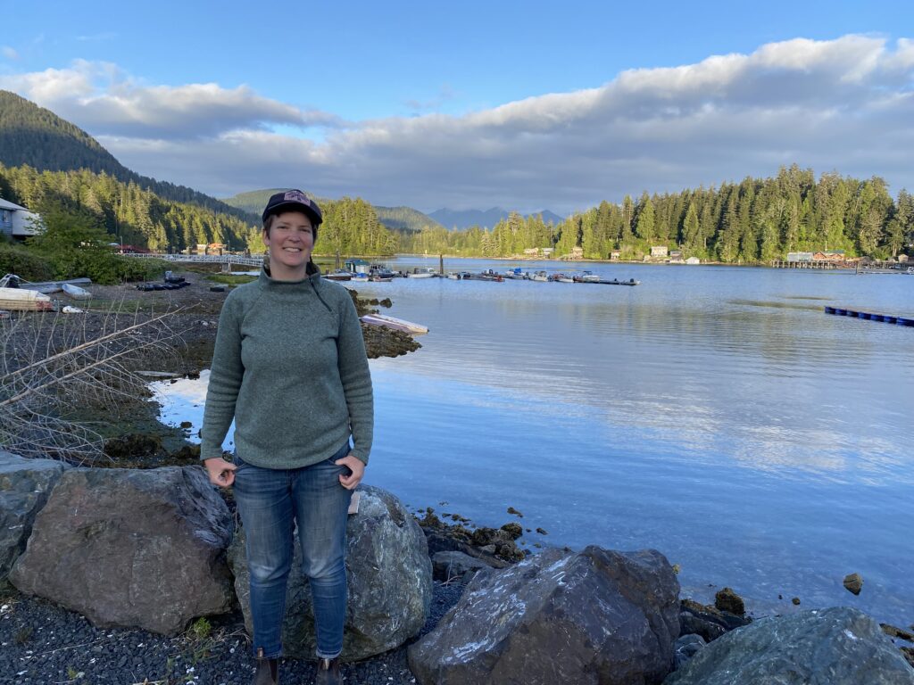 The author standing with a hat on with the village dock and inlet in the background.