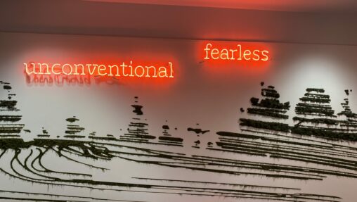 Art on a wall that says "unconventional" and "fearless" in neon red letters