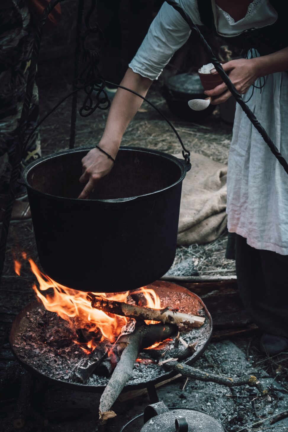 Woman's arm stirring a cauldron of soup over a fire