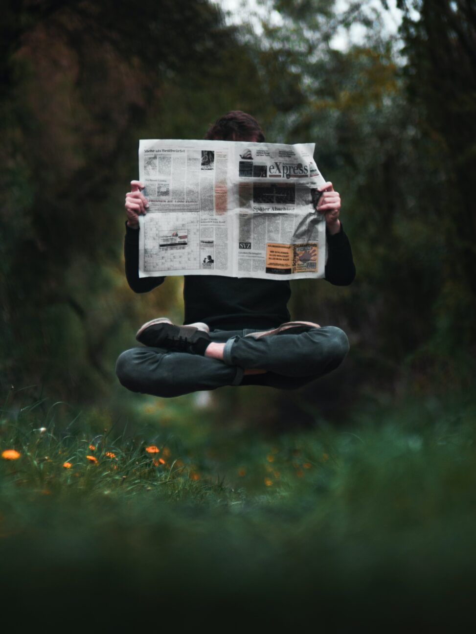 Person sitting cross legged reading a newspaper who appears to be floating above a grassy lawn