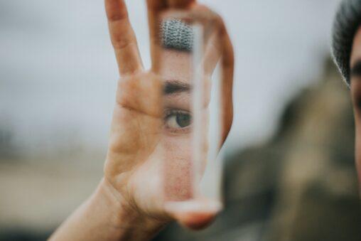 Hand holding a small piece of mirror with an eye reflected in it.